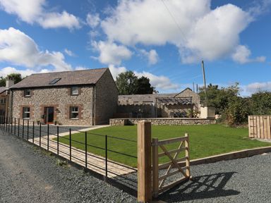 A stone house with a slate roof and fenced grassy yard with a wooden gate at The Stables in Penmon near Beaumaris