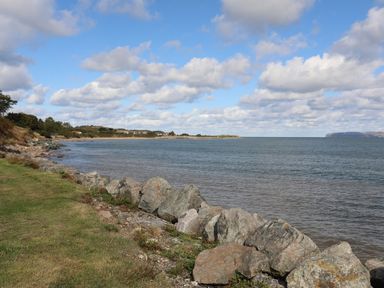 A shoreline with rocks grass and trees along a coast with water and clouds in the sky at The Stables in Penmon near Beaumaris