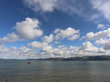 A large body of water with a small rocky outcrop and hills in the background under a sky with scattered clouds at The Stables in Penmon near Beaumaris