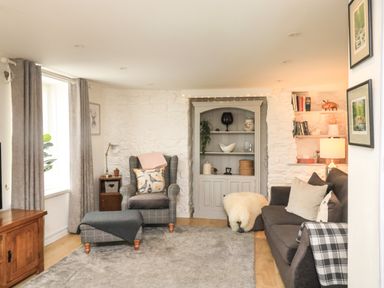 A living room with armchair ottoman sofa bookshelf and lamp at Hope Cottage in Buckfastleigh