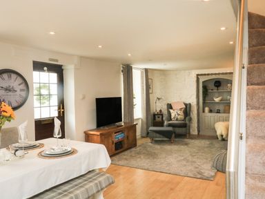 A living room and dining area with a dining table set for two a television armchair and bookshelf near stairs at Hope Cottage in Buckfastleigh