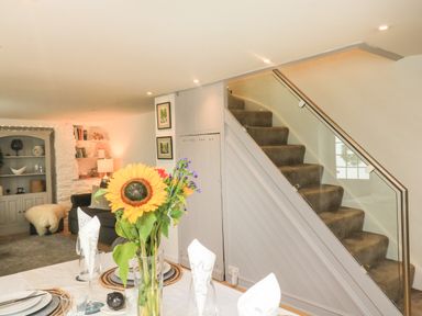 A dining table with flowers and place settings next to carpeted stairs with glass railing in a living area at Hope Cottage in Buckfastleigh