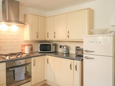 A kitchen with wooden cabinets a microwave kettle toaster gas stove oven and a Montpellier refrigerator at Hope Cottage in Buckfastleigh