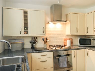 A kitchen with light wood cabinets and drawers a stainless steel oven and stove a microwave and a sink at Hope Cottage in Buckfastleigh