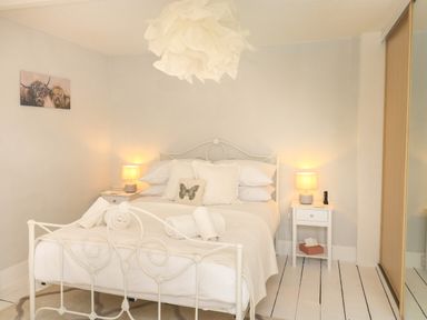 A bedroom with a white metal bed frame two bedside tables with lamps a butterfly pillow and a mirrored wardrobe at Hope Cottage in Buckfastleigh