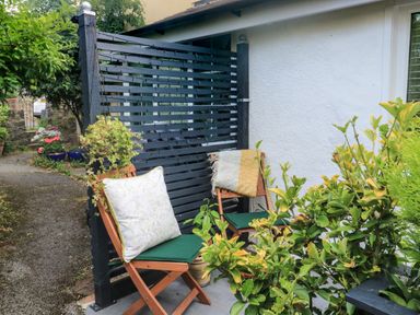 An outdoor seating area with two wooden chairs with cushions and a blanket near a black fence and green plants at Hope Cottage in Buckfastleigh