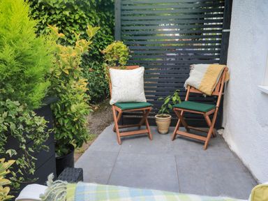 An outdoor seating area with two wooden chairs cushions and a small potted plant on tiled floor at Hope Cottage Buckfastleigh
