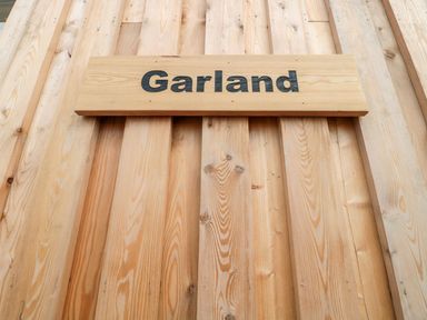 A wooden sign with the word Garland mounted on a vertical wooden plank wall at Garland in Nottington near Weymouth