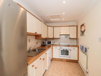 A kitchen with white cabinets wooden countertops a stainless steel refrigerator a sink an oven a microwave and a kettle at Garland in Nottington near Weymouth