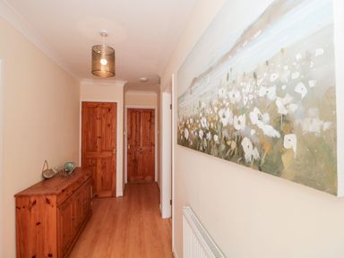 A hallway with wooden doors wooden sideboard a floral painting on the wall and a ceiling light at Garland in Nottington near Weymouth