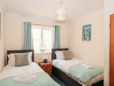 A bedroom with two single beds side by side separated by a wooden nightstand a window with curtains and a boat model on the windowsill and a painting on the wall at Garland in Nottington near Weymouth