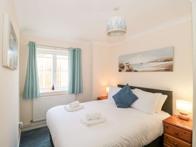 A bedroom with a double bed white linens blue curtains and landscape artwork at Garland in Nottington near Weymouth