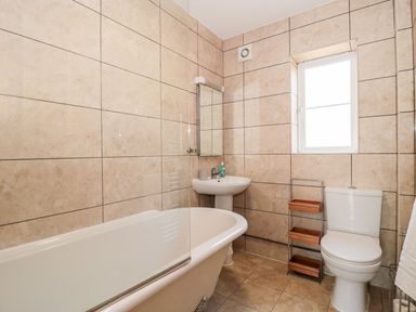 A bathroom with a bathtub sink toilet and a small shelving unit at Garland in Nottington near Weymouth