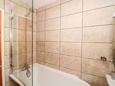A bathroom with a bathtub and shower area with tiled walls at Garland in Nottington near Weymouth