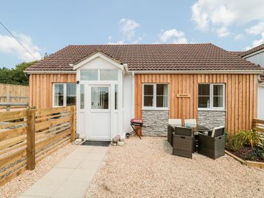 Exterior view of a wooden house with a tiled roof patio table and chairs and a barbecue at Garland in Nottington near Weymouth