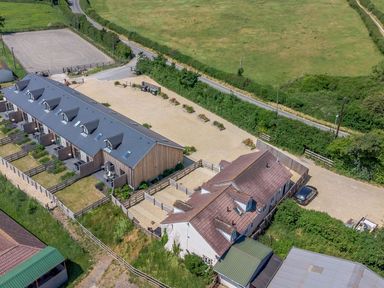 An aerial view of a residential area with fenced gardens gravel driveways multiple houses and green fields around Garland Nottington near Weymouth