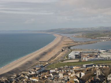 A coastal town with buildings near a long sandy beach and a body of water at Garland in Nottington near Weymouth