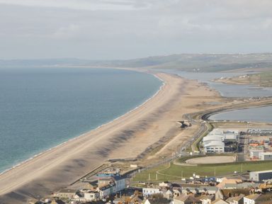 A coastline with a long sandy beach and a town with buildings near the water at Garland in Nottington near Weymouth