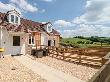 A house with outdoor seating and wooden fences overlooking green fields at Mellstock in Nottington near Weymouth
