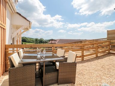 An outdoor patio area with a glass table and four chairs surrounded by a wooden fence at Mellstock Nottington near Weymouth