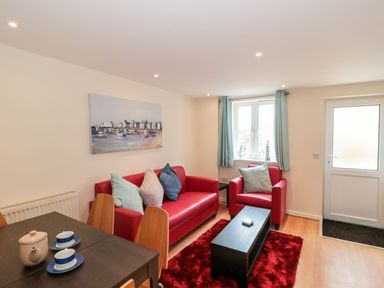 A living room with red sofa and armchair a black coffee table and dining table with cups at Mellstock in Nottington near Weymouth