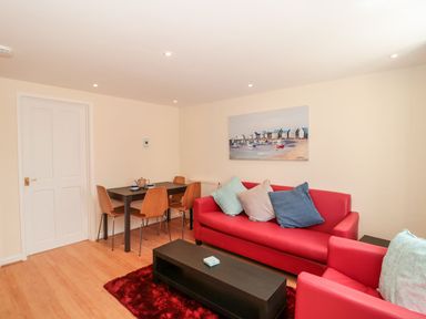 A living room with red sofas and a black coffee table next to a dining table with four chairs at Mellstock in Nottington near Weymouth