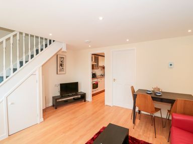 A living area with a staircase, television on a stand, dining table with chairs and a view into a kitchen at Mellstock in Nottington near Weymouth