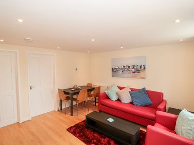 A living room with red sofa and armchair a black coffee table and dining table with wooden chairs at Mellstock in Nottington near Weymouth