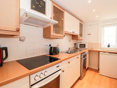 A kitchen with brown countertops white cabinets an electric stove a black toaster a microwave a dishwasher and a window at Mellstock in Nottington near Weymouth