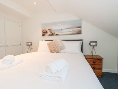 A bedroom with a double bed white linens towels bedside tables with lamps and a coastal painting above the bed at Mellstock in Nottington near Weymouth