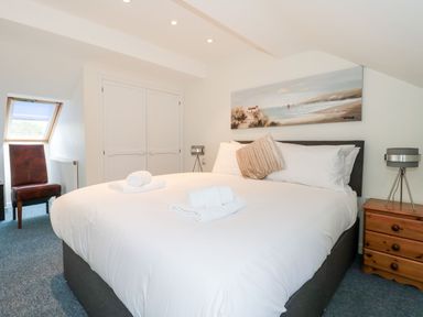 A bedroom with a large bed white bedding rolled towels a wooden bedside table two lamps a painting and a brown chair at Mellstock in Nottington near Weymouth