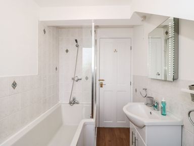 A bathroom with a bathtub and shower on the left and a sink with a mirror on the right at Mellstock in Nottington near Weymouth