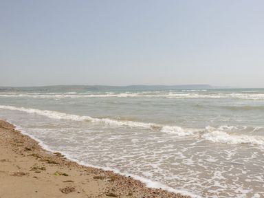 A sandy beach with small waves and distant hills at Mellstock in Nottington near Weymouth