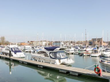 A marina with multiple docked boats and yachts and buildings in the background at Mellstock in Nottington near Weymouth