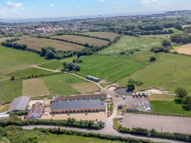 An aerial view of a rural property with several buildings green fields a round pen and a parking area near a village by the sea at Mellstock in Nottington near Weymouth