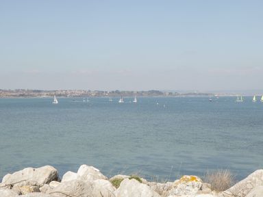 A view of a calm sea with sailboats and rocky shoreline at Mellstock in Nottington near Weymouth