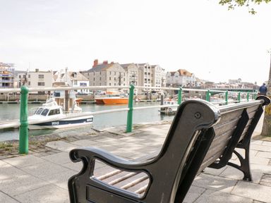 A bench overlooking a harbor with boats and buildings in the background at Mellstock in Nottington near Weymouth