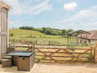 A wooden fenced patio area with garden furniture and a view of green fields and a hill at Emminster in Nottington near Weymouth