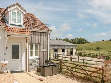 A house with a tiled roof and a small patio area with furniture next to a fenced rural farmland at Emminster in Nottington near Weymouth