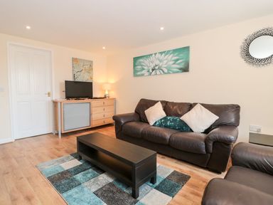 A living room with a brown leather sofa coffee table TV on a sideboard and wall art at Emminster in Nottington near Weymouth