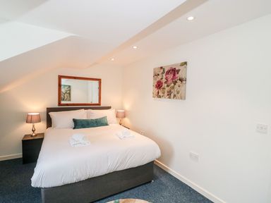 A bedroom with a double bed two bedside tables with lamps a wall mirror and floral artwork at Emminster Nottington near Weymouth