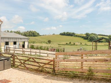 A fenced outdoor area with a stable building and a grassy field with a horse at Emminster in Nottington near Weymouth