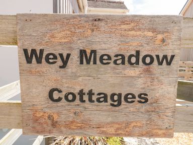 A wooden sign with the text Wey Meadow Cottages mounted on a wooden fence at Emminster in Nottington near Weymouth