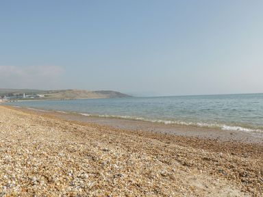 A pebble beach beside a calm sea with hills and buildings in the distance at Emminster in Nottington near Weymouth