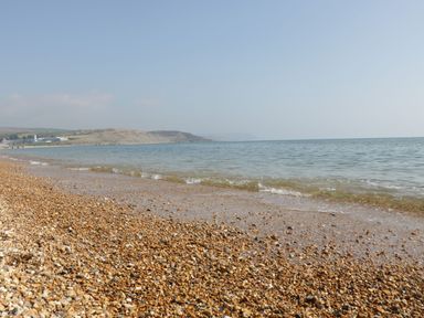 A pebble beach with gentle waves and a distant coastline at Emminster in Nottington near Weymouth