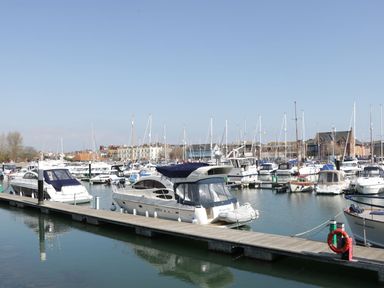 A marina with boats docked along wooden piers and buildings in the background at Emminster in Nottington near Weymouth