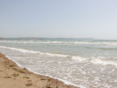 A beach with waves coming ashore and hills visible across the water at Emminster in Nottington near Weymouth