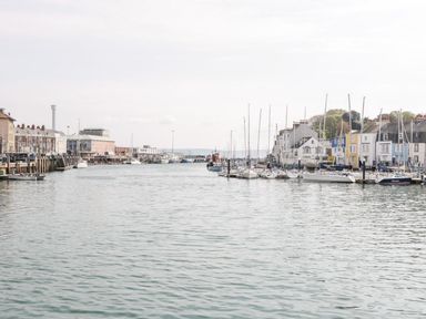 A harbor with boats docked along piers and buildings lining the waterfront at Emminster in Nottington near Weymouth