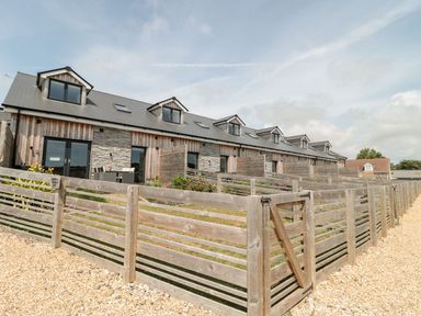 A row of connected holiday cottages with wooden fences and gravel path outside at Durbyfield in Nottington near Weymouth