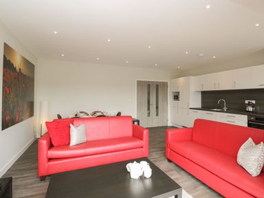 A living room with two red sofas and a black coffee table near a kitchen with white cabinets at Egdon Heath in Nottington near Weymouth